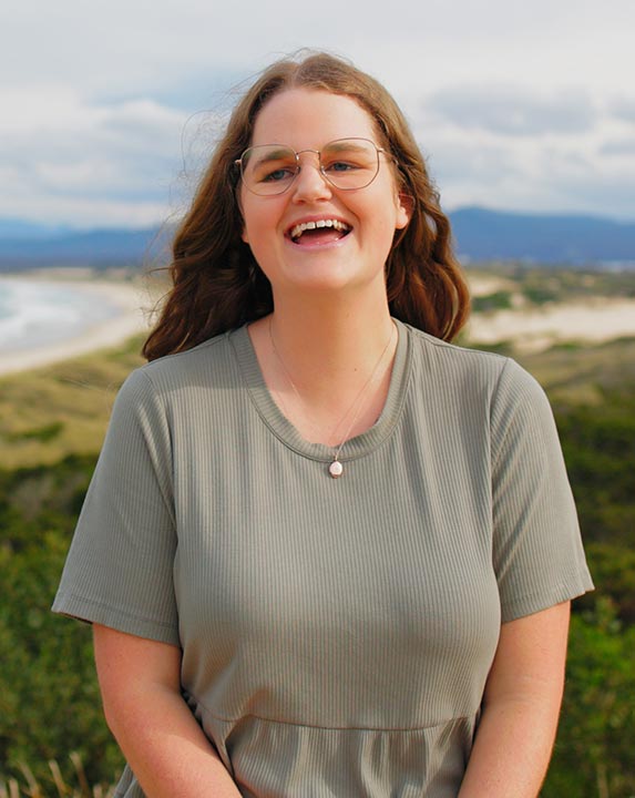 Georgia, a young person who has benefited from Canteen's free cancer support services, standing in front of the ocean